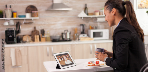 Business woman on a video call with her mother during breakfast. Using modern online internet web technology to chat via webcam videoconference app with relatives, family, friends and coworkers