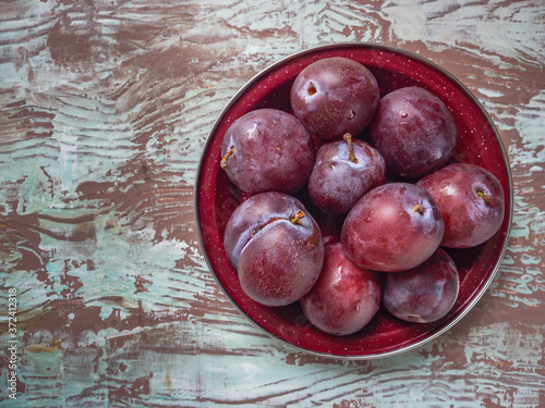 Plate with red plums on brown wooden table top view plan with place photo