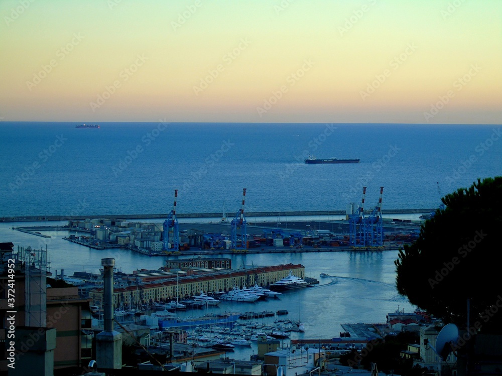 Genoa, Italy – August 5, 2020: Aerial view of shipping and container terminal, in the port of Genoa, and panoramic view to the other side of the city without the seaside, Stadium and residences.