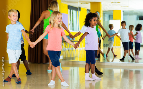 Fototapeta Naklejka Na Ścianę i Meble -  Group of kids with their teacher holding hands and dancing in circle in dance school