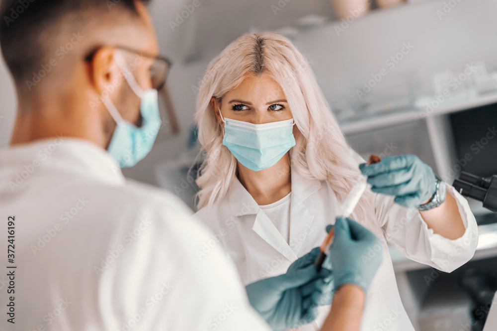 Two dedicated medical workers standing in laboratory and holding test tube with blood sample. Two dedicated medical workers standing in laboratory and holding test tube with blood sample.