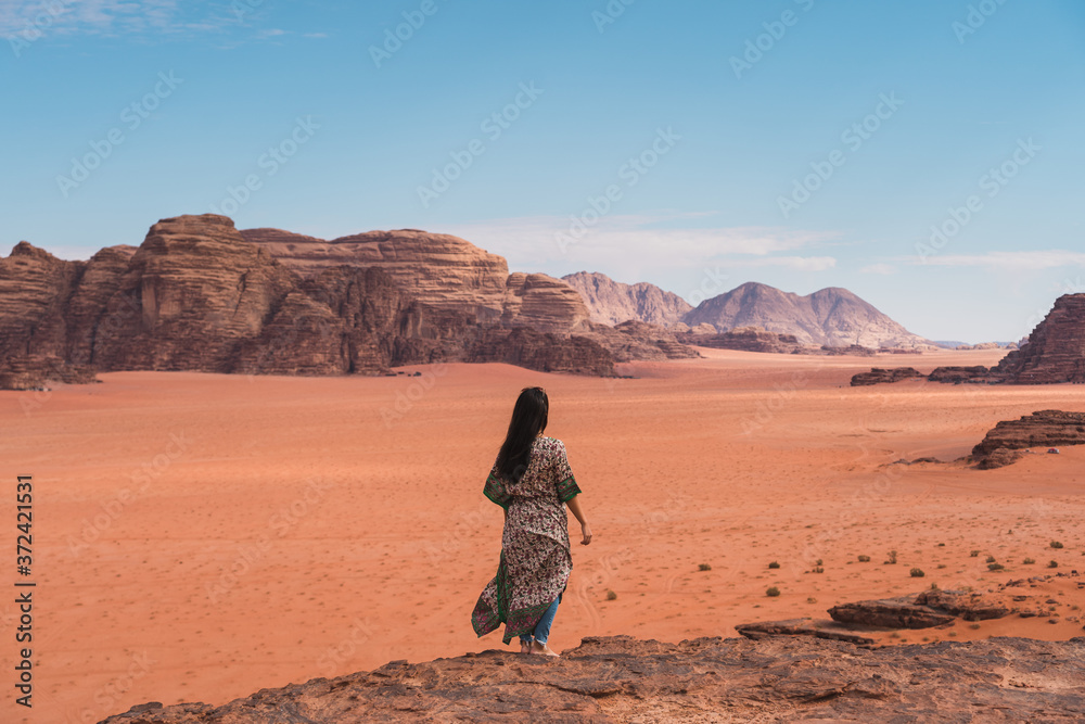 Young Asian traveller with local Arab dress standing on top of mountain and enjoying landscape of Wadi Rum desert, Jordan, Arab