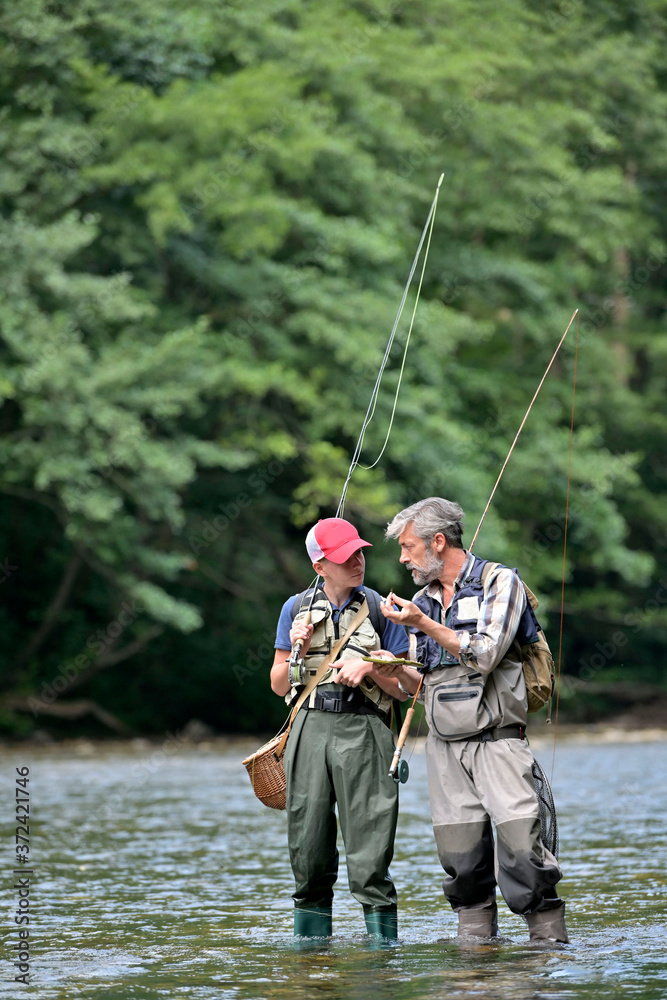 A father and his son fly fishing in summer on a beautiful trout river with clear water