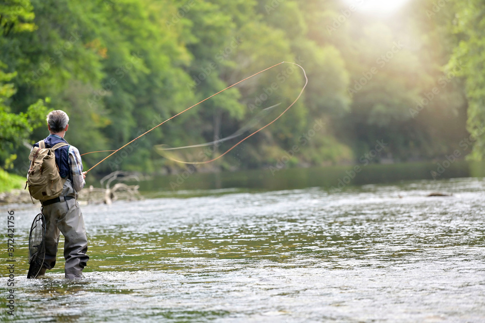 Man fly fishing in the summer in a beautiful river with clear water Man fly fishing in the summer in a beautiful river with clear water