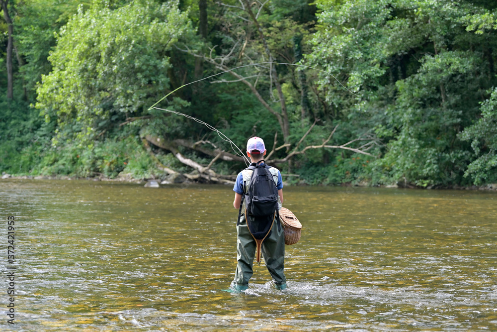 young boy fly fishing in summer in a beautiful river with clear water young boy fly fishing in summer in a beautiful river with clear water