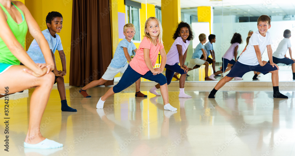 Preteen boys and girls practicing dance, stretching with female trainer in dance hall.