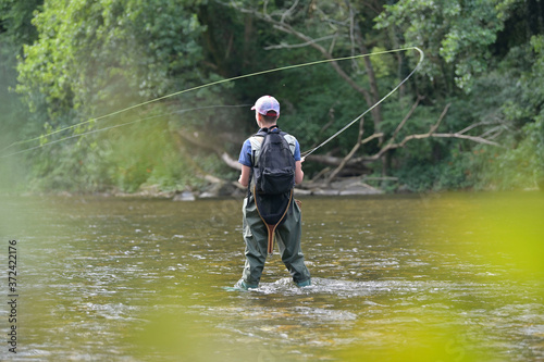 young boy fly fishing in summer in a beautiful river with clear water