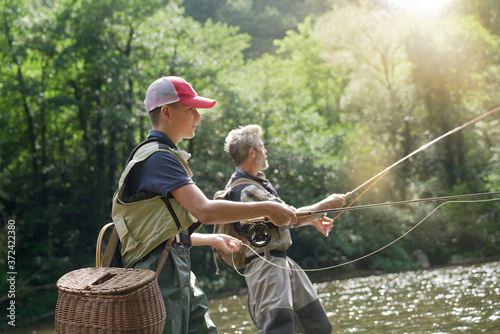 Tablou canvas A father and his son fly fishing in summer on a beautiful trout river with clear