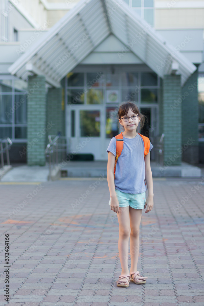 Cute happy schoolgirl with backpack leaving school