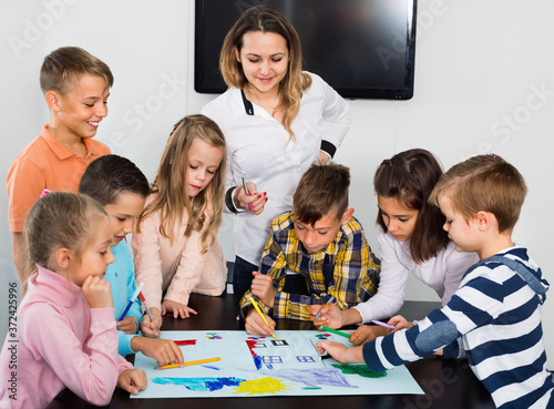 Cute happy children with teacher drawing together in classroom