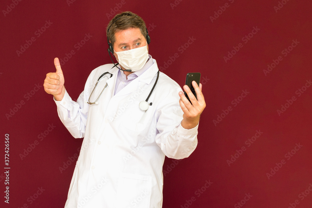 Young caucasian doctor with stethoscope, medical mask talking with patient online red background Young caucasian doctor with stethoscope, medical mask talking with patient online red background