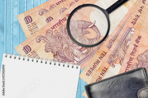 10 Indian rupees bills and magnifying glass with black purse and notepad. Concept of counterfeit money. Search for differences in details on money bills to detect fake