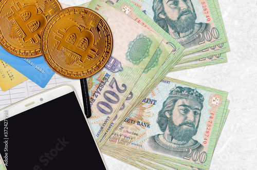 200 Hungarian forint bills and golden bitcoins with smartphone and credit cards. Cryptocurrency investment concept. Crypto mining or trading photo