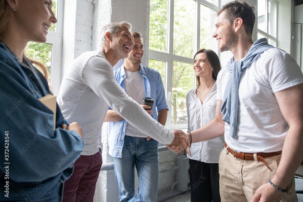 Welcome to our team! Business men in smart casual wear shaking hands while working in the creative office