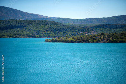 Panoramic view on Sainte Croix lake in South of France. Artificial lake from 1973. Panorama on lake with view on little Provence town. Perfect quiet water and blue sky. Moutains from Alps