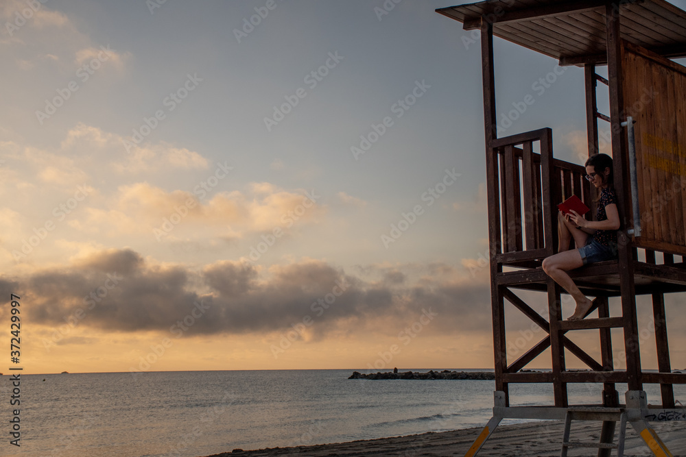 A woman reading in the beach during sunrise