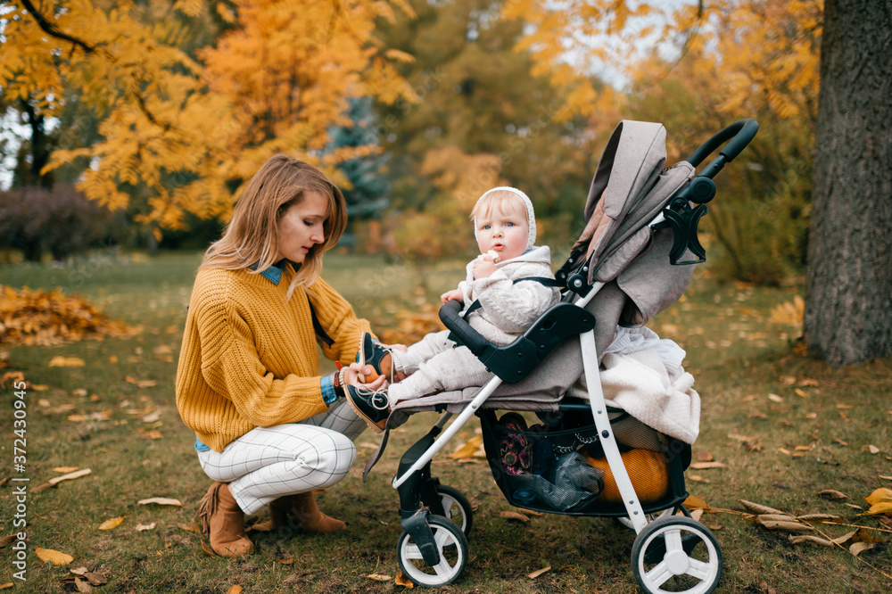 Magnetic little baby in a stroller outside in the fall with its lovely happy mum