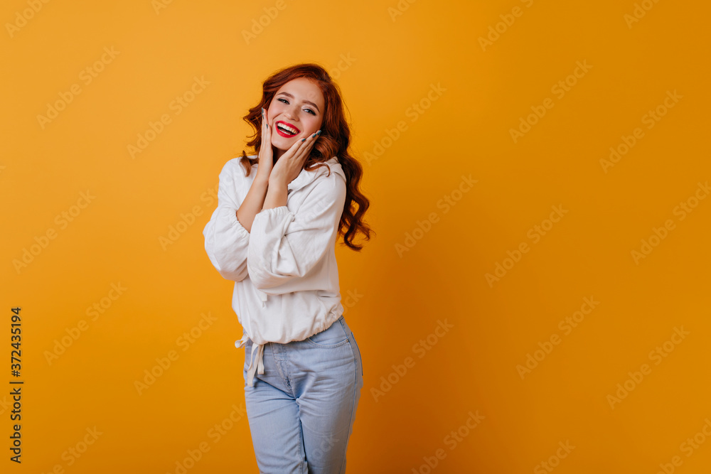 Amazing long-haired woman smiling on yellow background. Gorgeous ginger female model posing in white sweater. Amazing long-haired woman smiling on yellow background. Gorgeous ginger female model posing in white sweater.