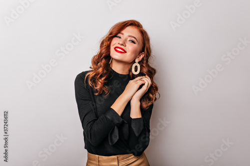 Debonair stylish woman in black blouse smiling to camera. Studio shot of graceful european girl wears golden earrings.
