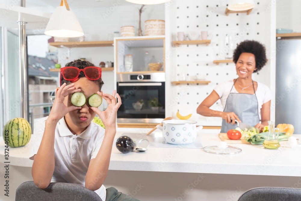Boy having fun with cucumber slices while mother is cooking food Boy having fun with cucumber slices while mother is cooking food