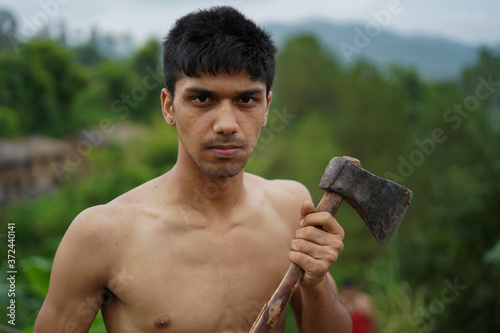 Young handsome shirtless boy holding axe in his hands.