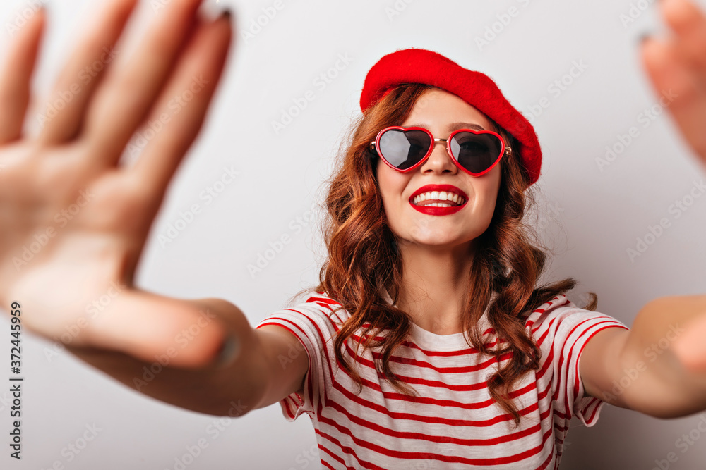 Blithesome caucasian girl in red beret having fun in studio. Enchanting ginger female model posing in sunglasses. Blithesome caucasian girl in red beret having fun in studio. Enchanting ginger female model posing in sunglasses.