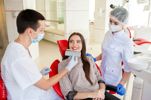 A dentist with an assistant, pick up the color of teeth to a beautiful girl. photo