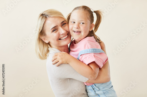 Foto Portrait of happy mother embracing her daughter with down syndrome against the w