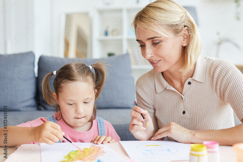 Little girl sitting at the table and painting a picture together with her mother at home Little girl sitting at the table and painting a picture together with her mother at home