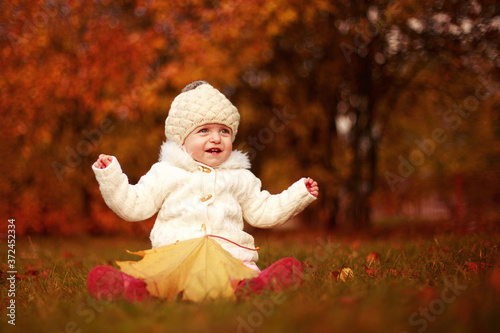 beautiful little baby girl sitting with a big leaf at autumn park