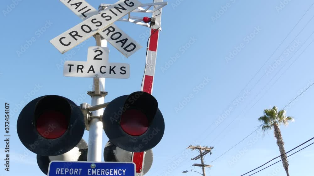 Level crossing warning signal in USA. Crossbuck notice and red traffic light on rail road intersection in California. Railway transportation safety symbol. Caution sign about hazard and train track.