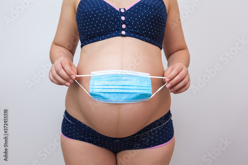 A pregnant woman holds a medical mask against the background of her stomach