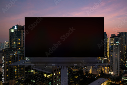 Blank black road billboard with Bangkok cityscape background at night time. Street advertising poster, mock up, 3D rendering. Front view. The concept of marketing communication to sell idea.