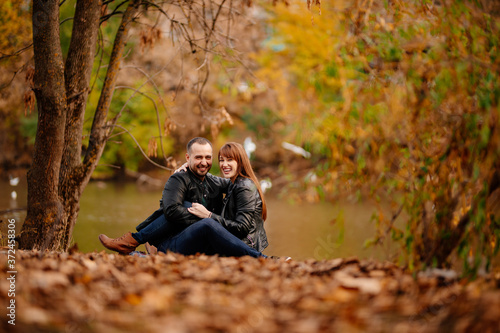 couple sitting on Bank of river in autumn park.