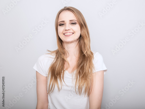 Pretty toothy laughing young woman with fair blond long hair in casual dress. Studio shot of good looking beautiful woman isolated against grey studio wall