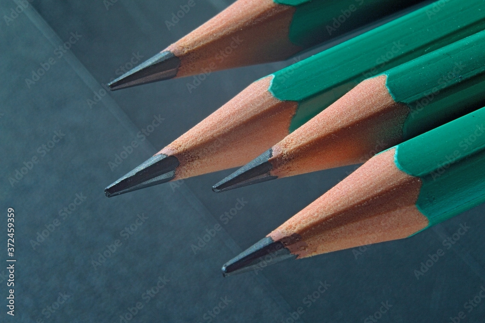 Green sharpened wooden pencils with black lead on a dark textured background. close-up. Green sharpened wooden pencils with black lead on a dark textured background. close-up.