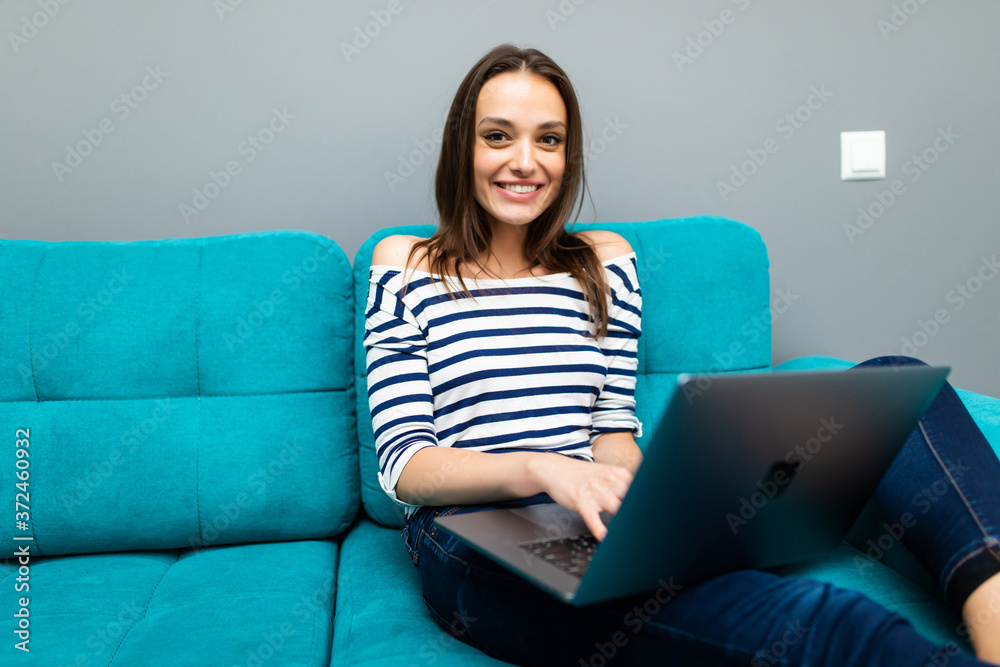 Happy pretty woman using laptop sitting on sofa