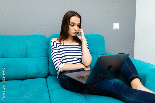 Free Download home, technology and internet concept. Young smiling woman with laptop computer sitting on couch at home - GFXLoad
