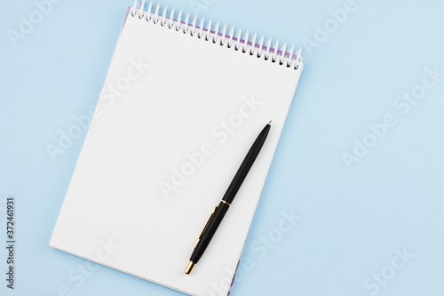 White blank notebook with a black branded pen on a light blue background. View from above. Photo concept.