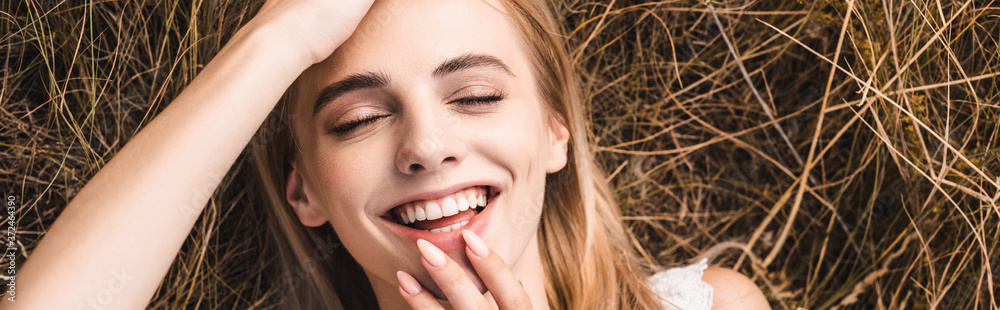 Obraz premium website header of excited young woman touching lips and forehead while lying on green grass, top view