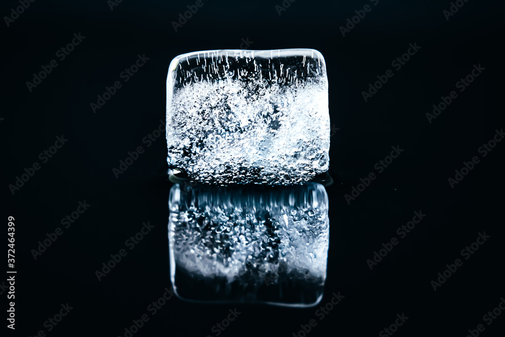 Melting ice cube with reflection on dark background Melting ice cube with reflection on dark background
