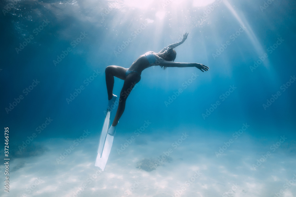 Attractive woman freediver glides and posing over sandy bottom with fins.