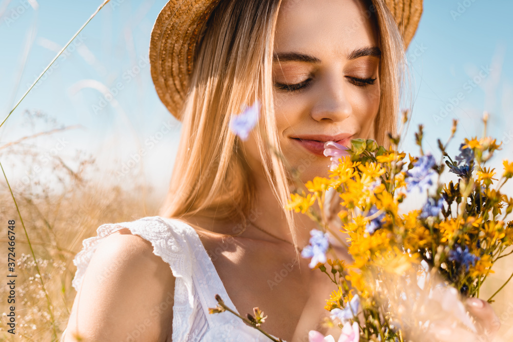 selective focus of sensual woman in straw hat smelling bouquet of wildflowers with closed eyes selective focus of sensual woman in straw hat smelling bouquet of wildflowers with closed eyes