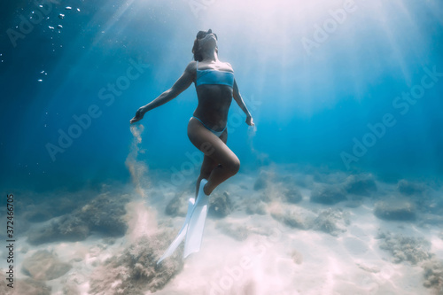 Attractive woman freediver glides and posing with sandin hands over sandy bottom with white fins.