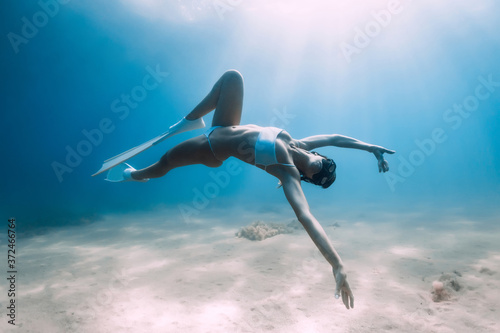 Attractive woman freediver glides and posing over sandy bottom with fins.