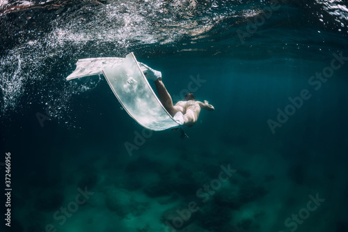 Woman freediver with white fins glides underwater in transparent sea