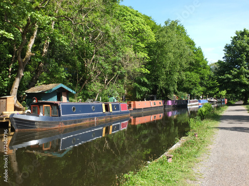 canal boats moored opposite the path on the rochdale canal near hebden bridge surrounded by trees in summer sunlight