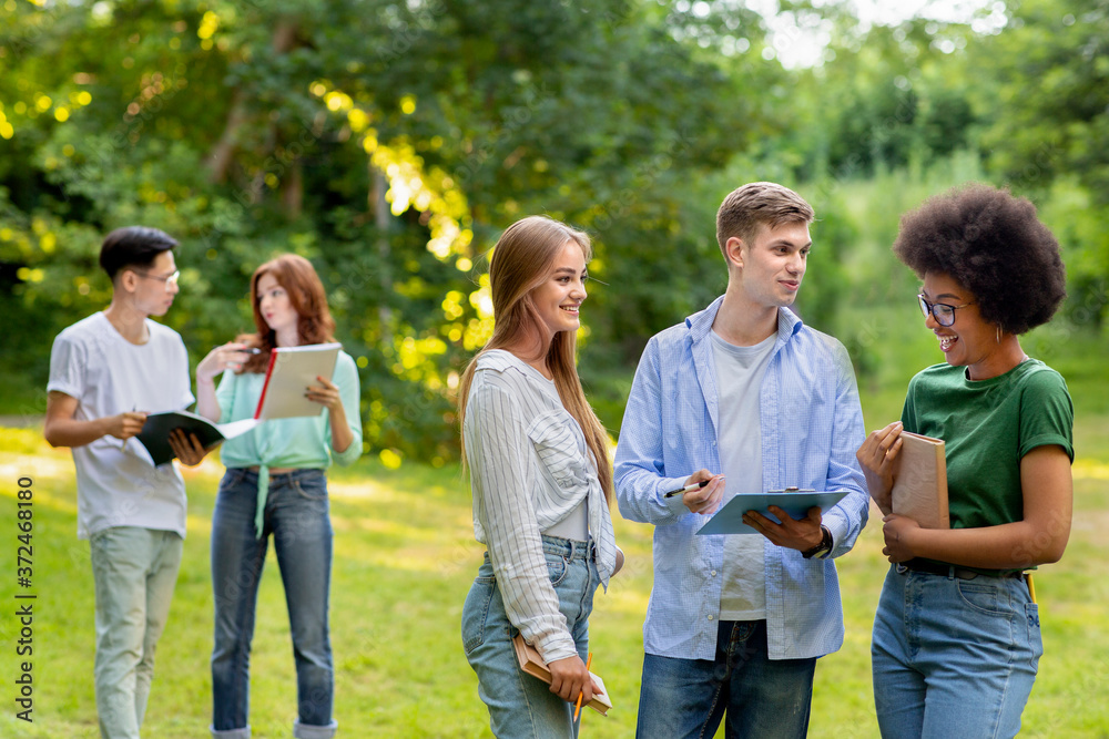 Multi ethnical teenage classmates resting outdoors between classes, chatting and smiling together Multi ethnical teenage classmates resting outdoors between classes, chatting and smiling together