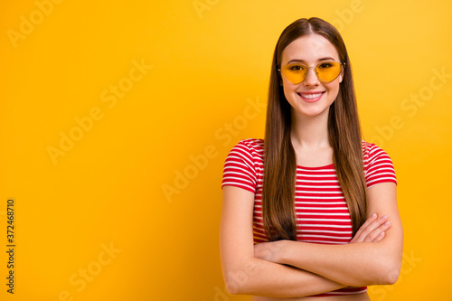 Photo of pretty lovely self-assured young girl folded hands smiling leadership coach ready start training empty space wear sun specs striped white red shirt bright yellow color background