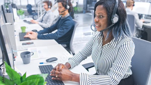 Beautiful Young Female Customer Service Operator Working in a Busy Modern Call Center with Diverse Multicultural Team of Office Specialists Wearing Headsets and Taking Calls. 